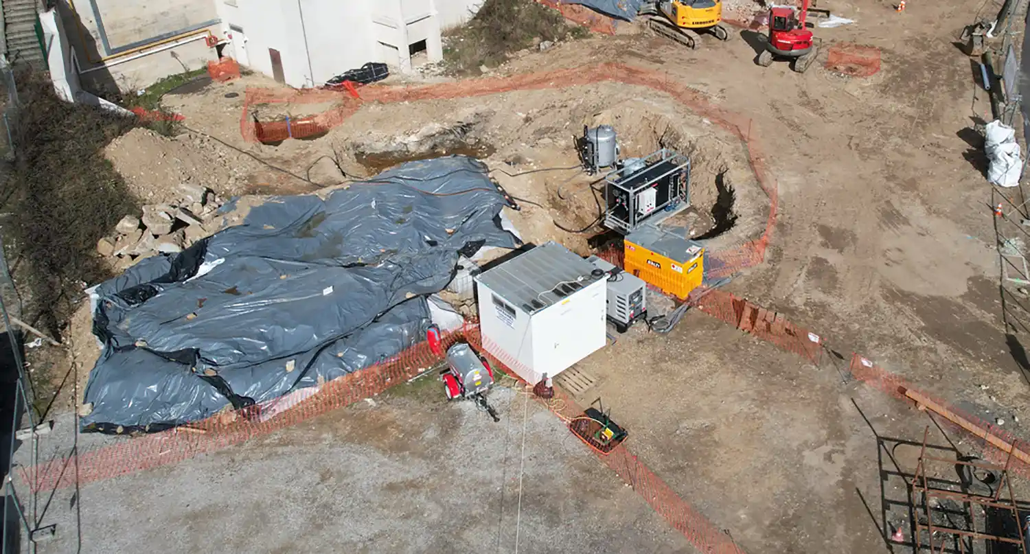 Chantier de construction avec bâches grises, équipements industriels, clôture orange et engins de chantier rouges et jaunes à Annonay.